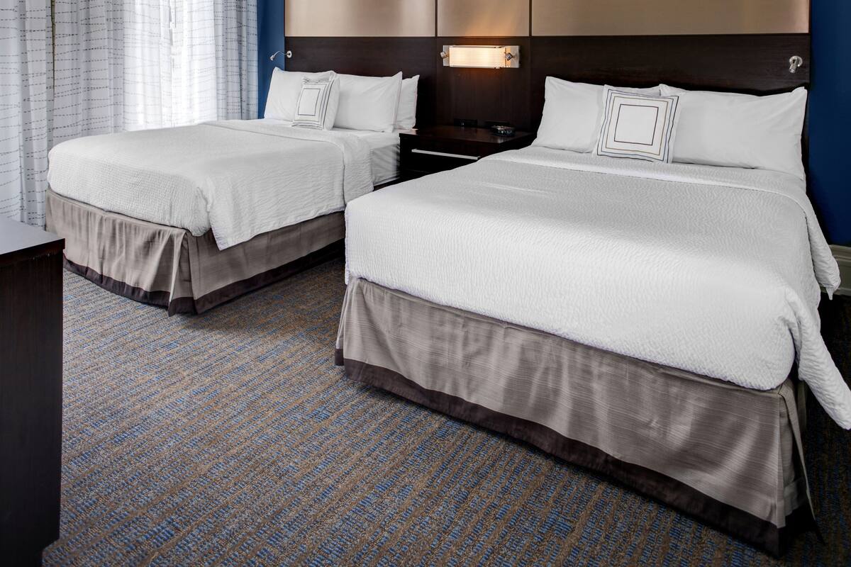 A hotel room with two beds, a desk, and a nightstand.