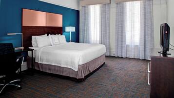 A hotel room with a large bed, a desk with a chair, a TV, and a window with curtains.