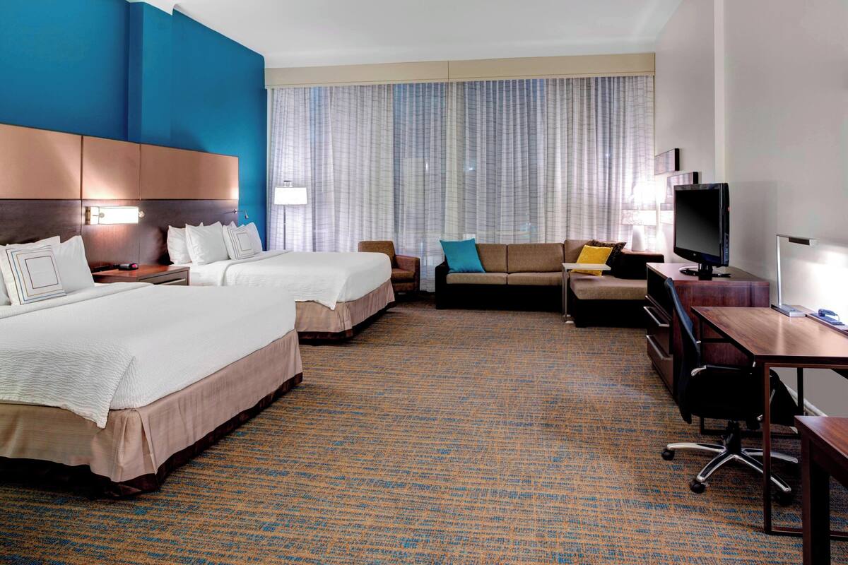 A hotel room with two beds, a sofa, a desk, and a television.