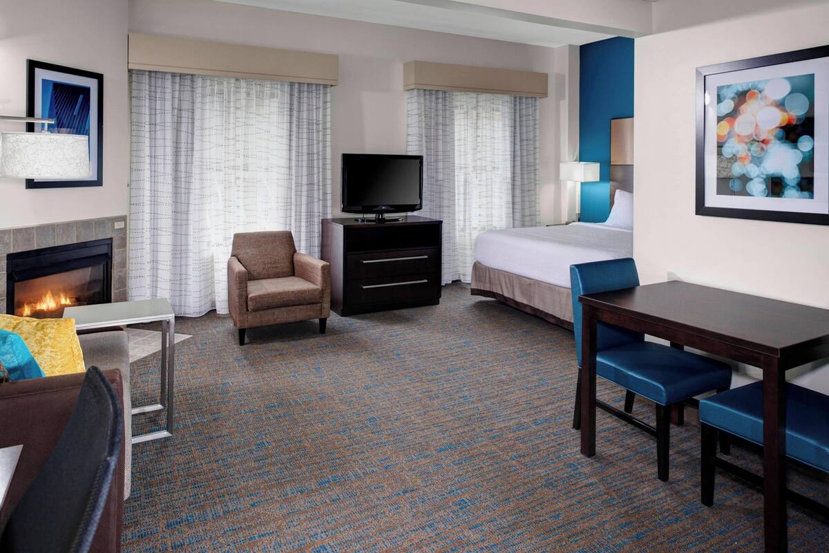 A hotel room with a fireplace, a TV, a bed, a desk, and a chair.
