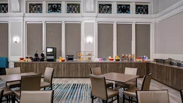A hotel dining area with a long counter, multiple seating arrangements, and a decorative stained glass window above.