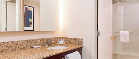 A bathroom with a granite countertop, a sink, a mirror, and a glass shower enclosure.
