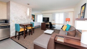 A hotel room with a bed, desk, TV, dining area, and kitchenette.