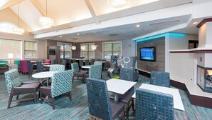A modern hotel lobby with seating areas, a television, and a fireplace.