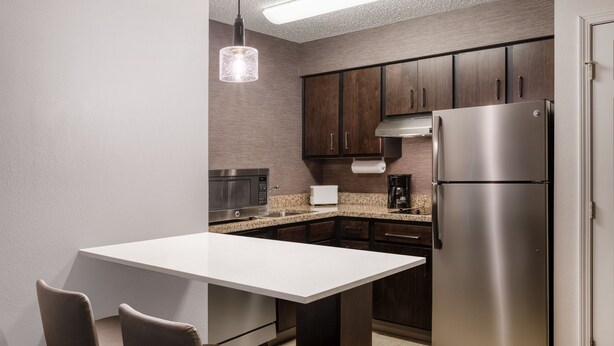 A modern kitchen with dark wooden cabinets, stainless steel appliances, and a white countertop.