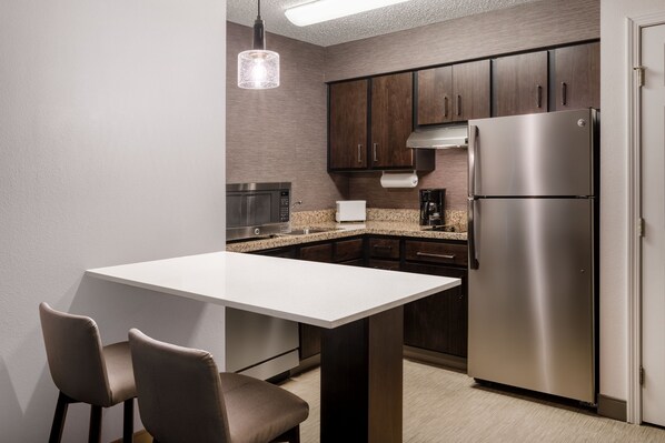 A modern kitchen with dark wooden cabinets, stainless steel appliances, and a white countertop. - Residence Inn by Marriott Boulder Broomfield (Louisville)