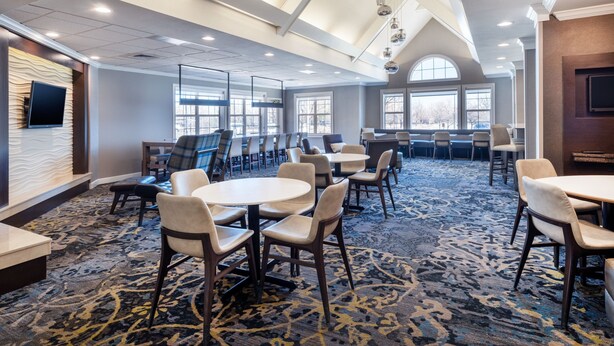 A hotel conference room with multiple tables and chairs, large windows, and a high ceiling with recessed lighting. - Residence Inn by Marriott Boulder Broomfield (Louisville)