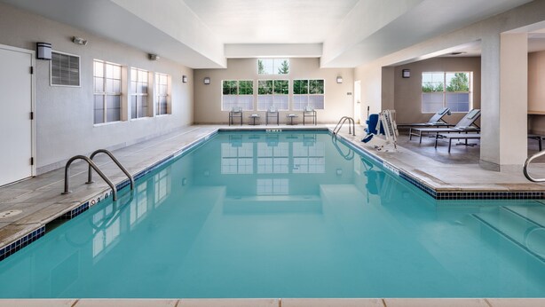 An indoor swimming pool with clear glass walls, a tiled floor, and a few lounge chairs and tables. - Residence Inn by Marriott Boulder Broomfield (Louisville)