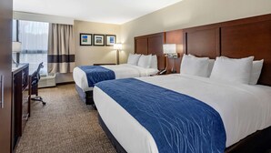 A hotel room with two beds, a desk, a chair, a lamp, and a window with curtains.