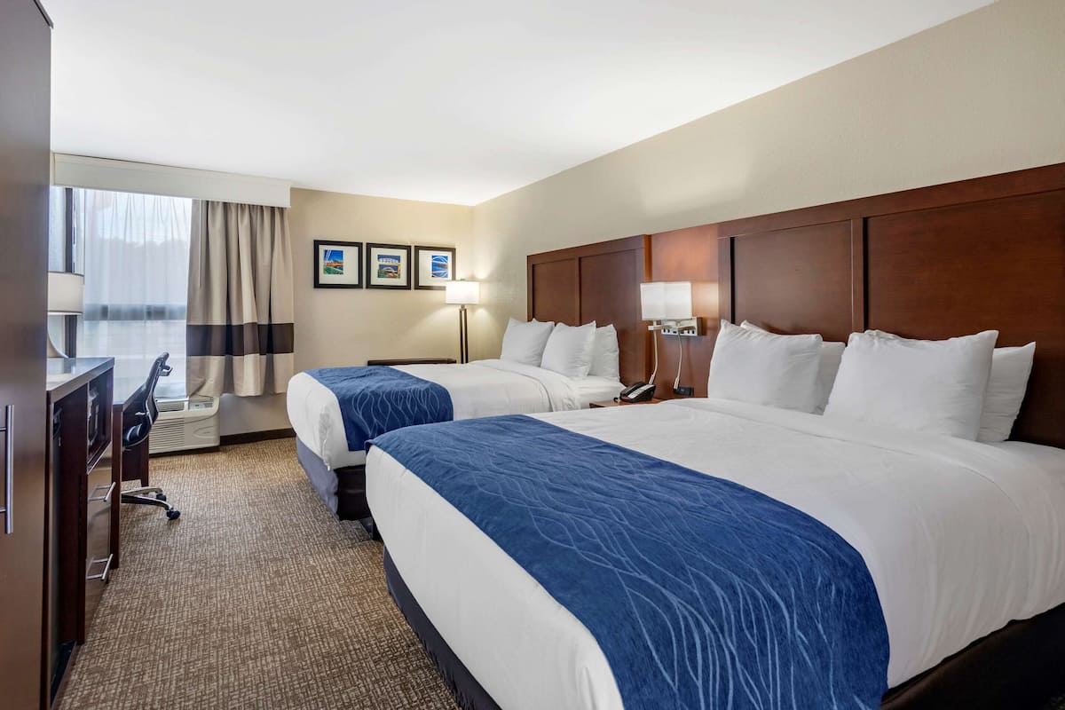 Une chambre d’hôtel avec deux lits, un bureau, une chaise, une lampe et une fenêtre avec des rideaux.