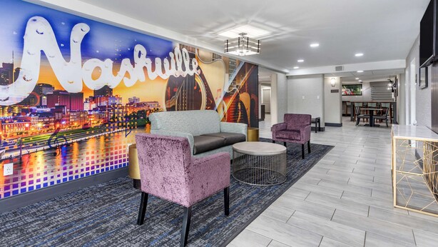 A lobby with a cityscape mural, a seating area with a sofa and armchairs, a dining area, and a modern staircase.