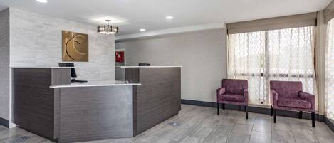 A reception area with a modern desk, two patterned chairs, and a large window with curtains.