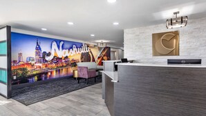 A hotel reception area with a cityscape mural, a reception desk, and a staircase.