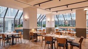 A modern restaurant with wooden flooring, multiple dining tables, and chairs. Large windows allow natural light and views of the outside. - Rydges North Sydney (North Sydney)