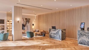 A modern hotel lobby with a wooden herringbone floor, a reception desk with marble top, and a seating area with sofas and chairs. - Rydges North Sydney (North Sydney)