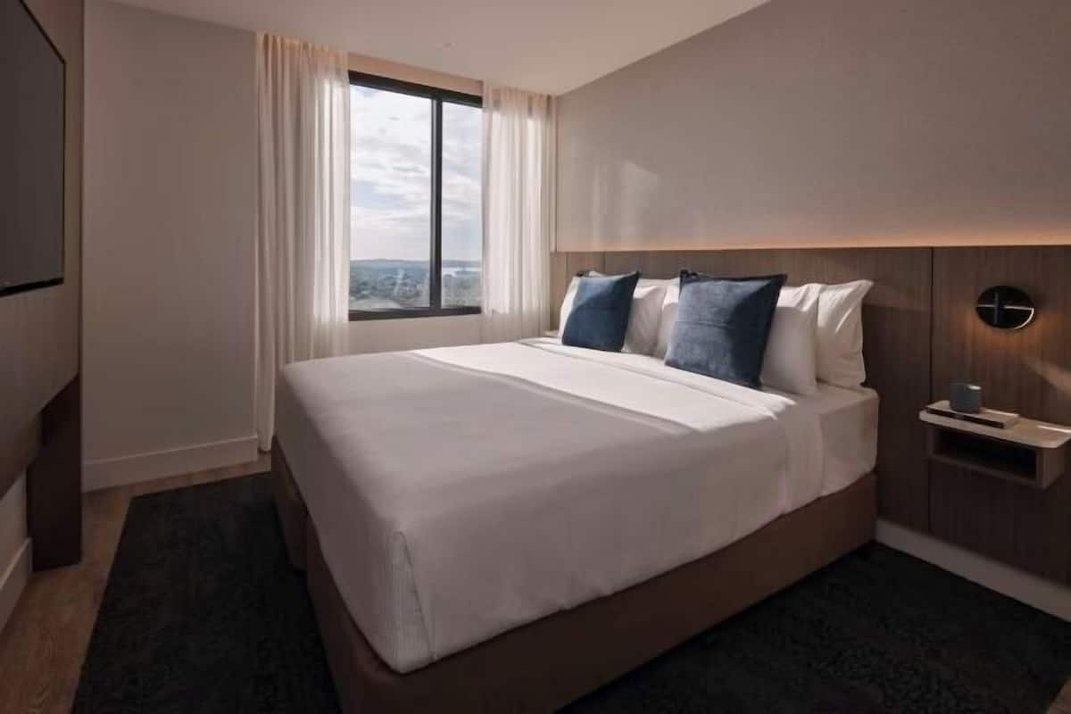 A hotel room with a large bed, a nightstand, a wall-mounted clock, and a window with curtains.