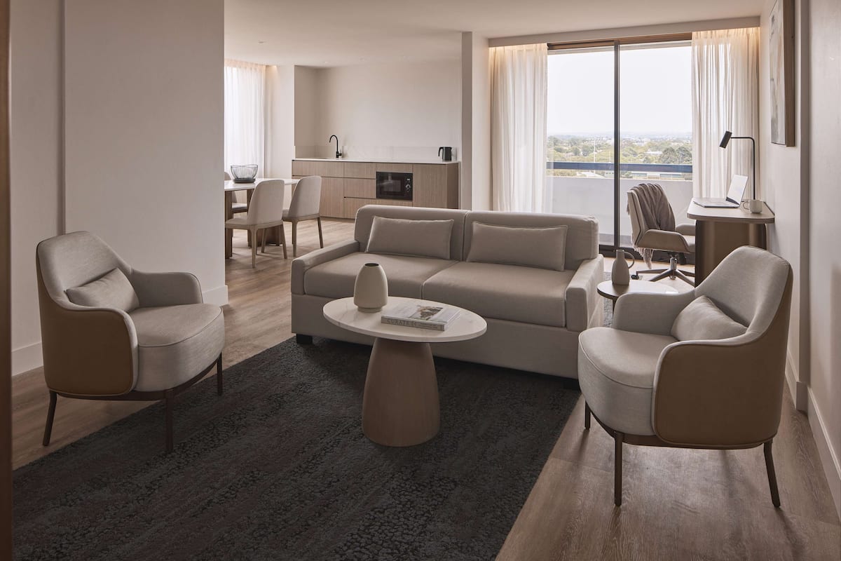 A modern living room with a sofa, two armchairs, a coffee table, and a dining area in the background.