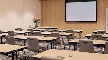A conference room with multiple tables and chairs, a projector screen, and a floral arrangement.