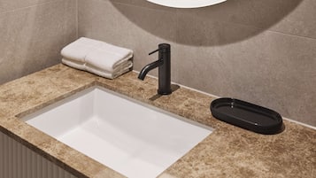 Baño con lavamanos blanco, grifo negro y una pila de toallas.