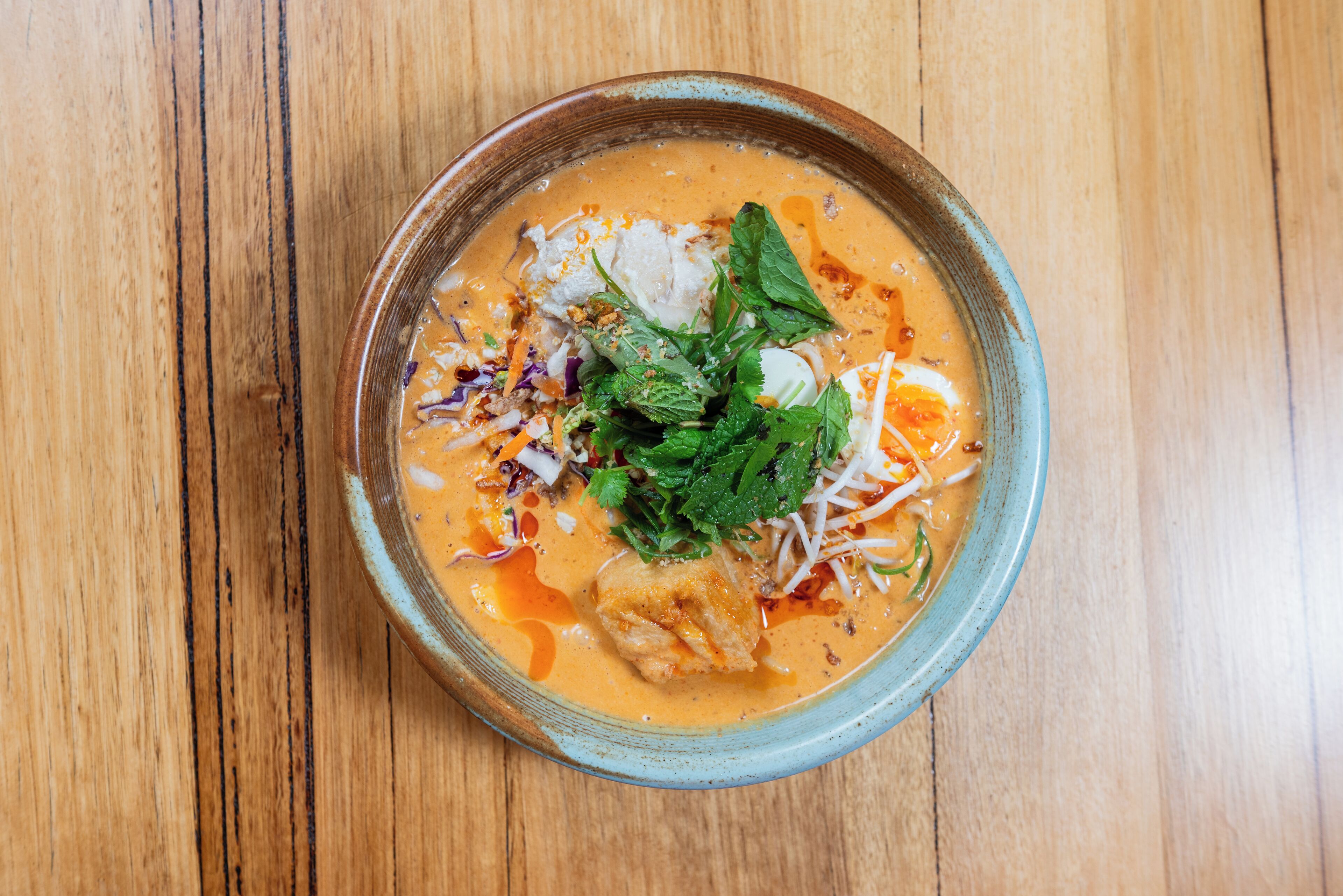 A bowl of soup with various toppings on a wooden table.