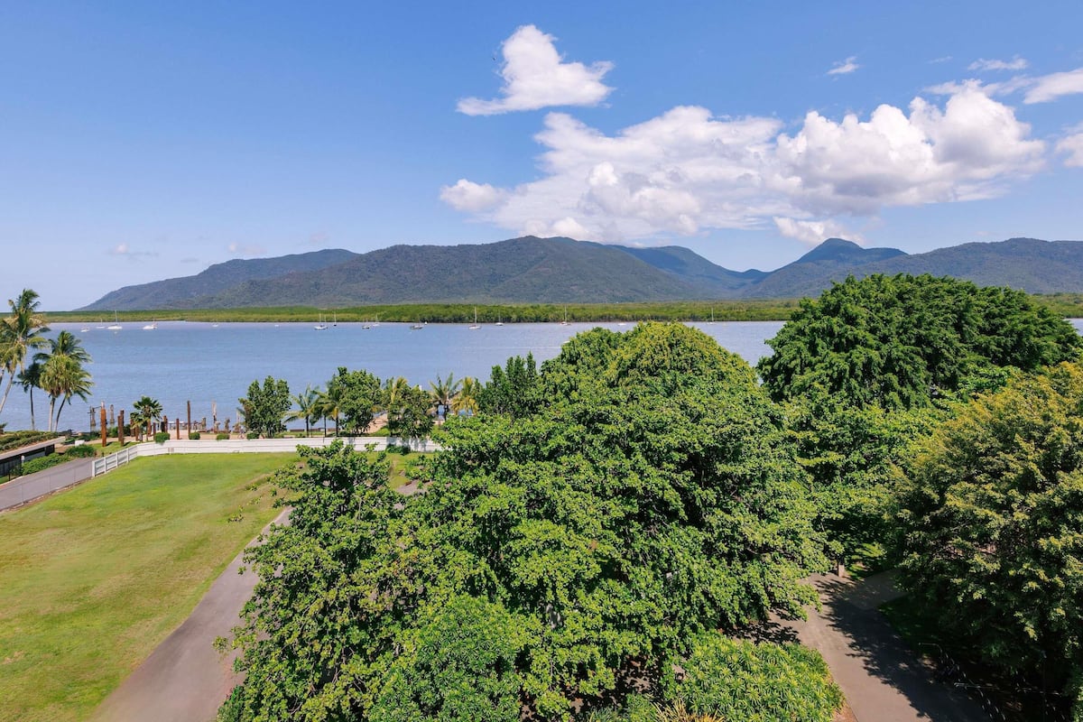 A coastal landscape with a clear view of the sea, lush greenery, and distant mountains.