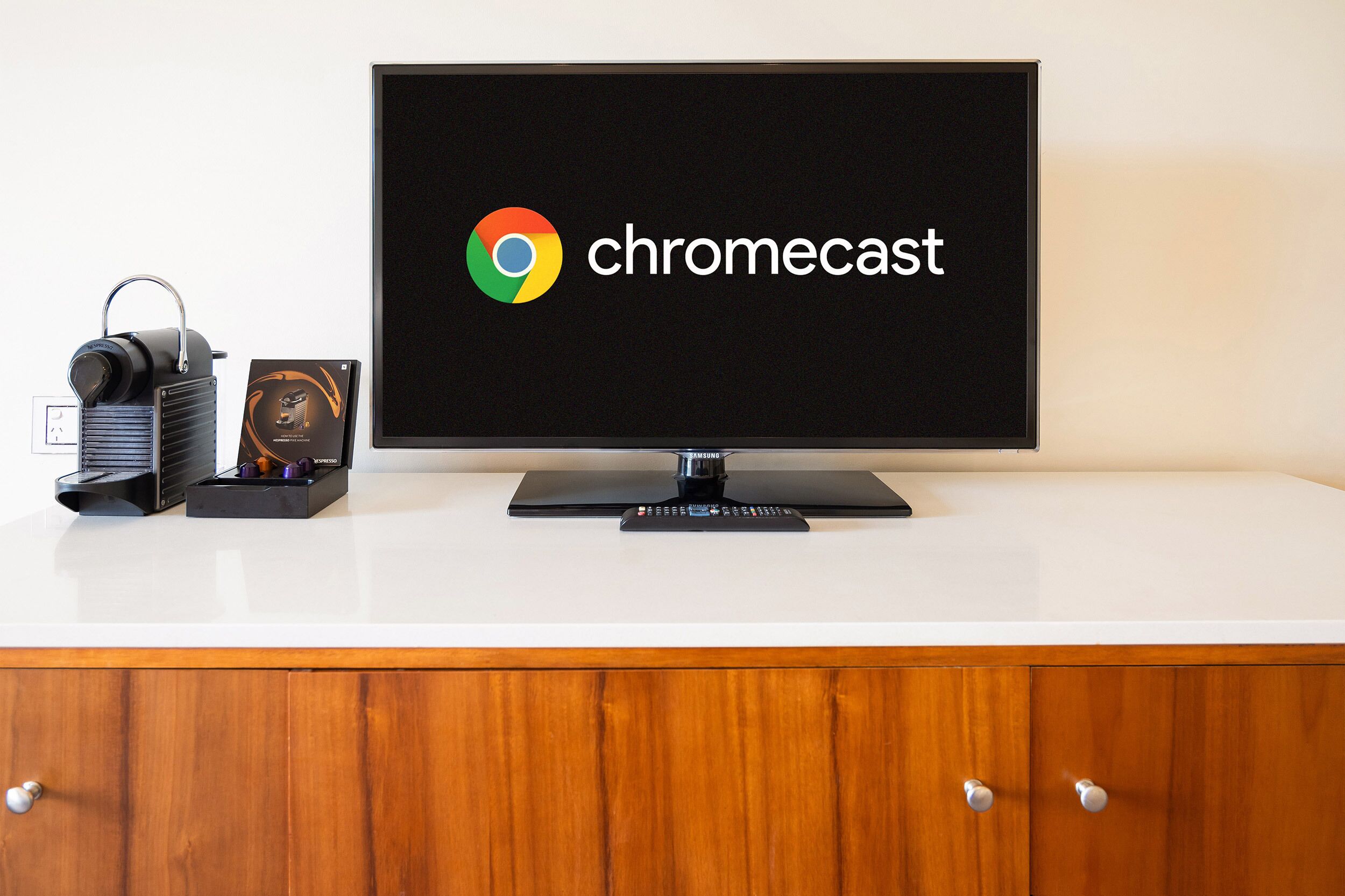Ein Flachbildfernseher mit Chromecast-Logo auf dem Bildschirm, platziert auf einer weißen Oberfläche mit einem Holzkasten darunter.