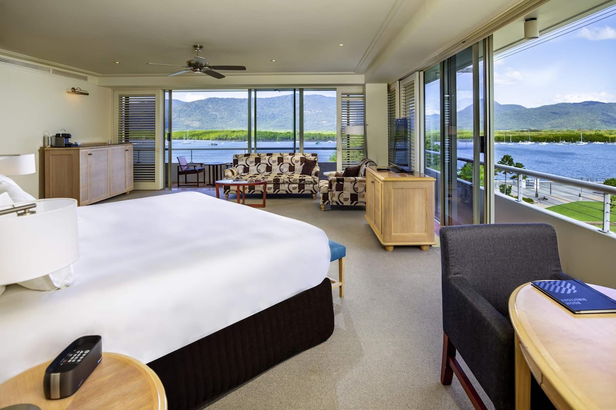 Hotelkamer met een groot bed, een bureau, een stoel, een bank en een balkon met uitzicht op een meer en bergen.