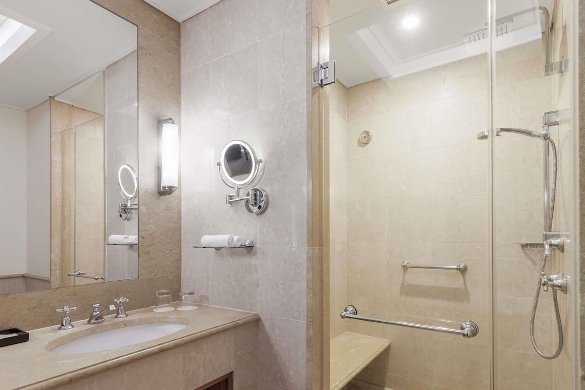 A modern bathroom with a large mirror, two sinks, a shower with a glass door, and a towel rack.