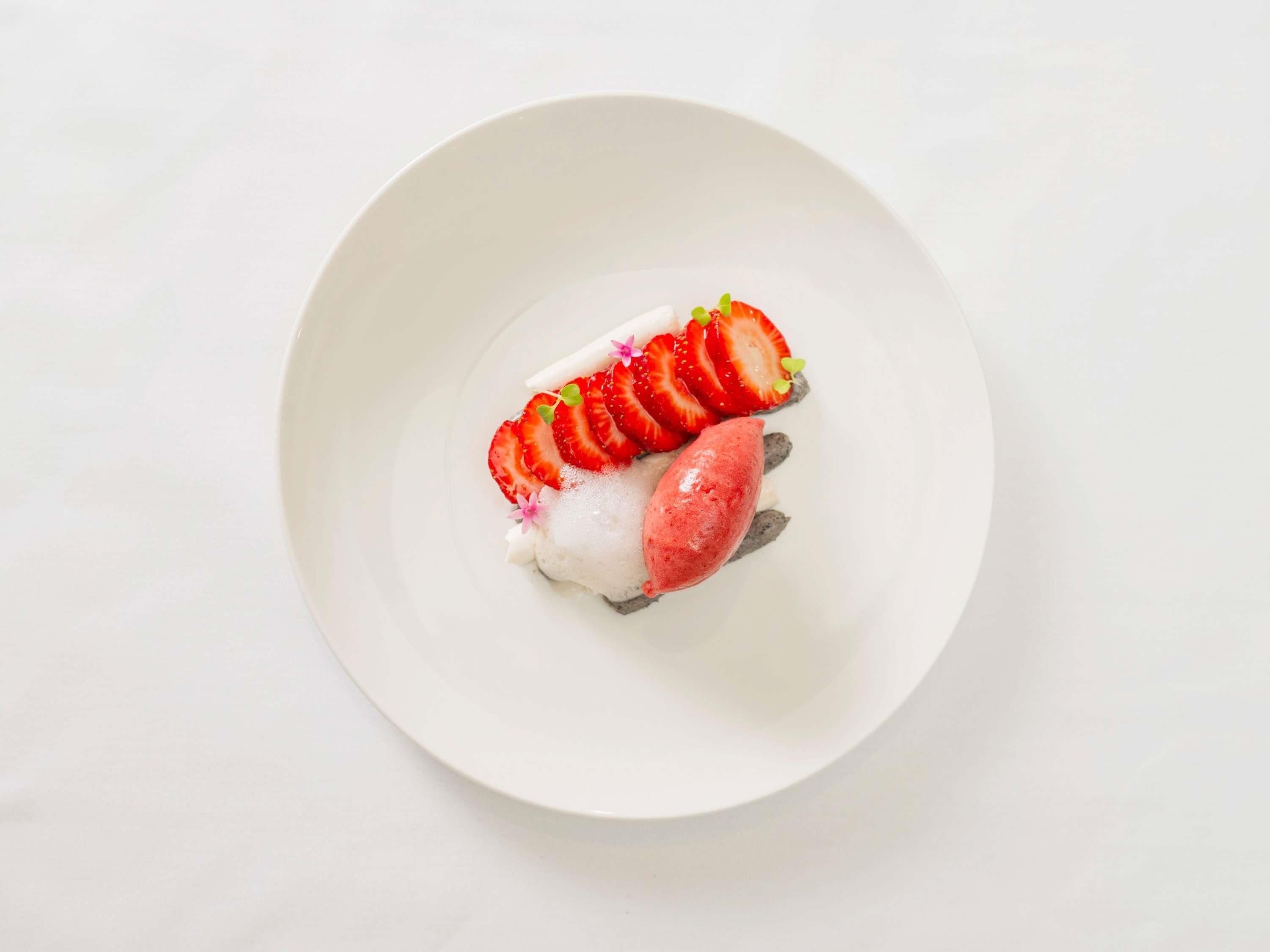 Une assiette blanche contenant un dessert composé d’une base blanche, d’une garniture rouge et de tranches de fraises.