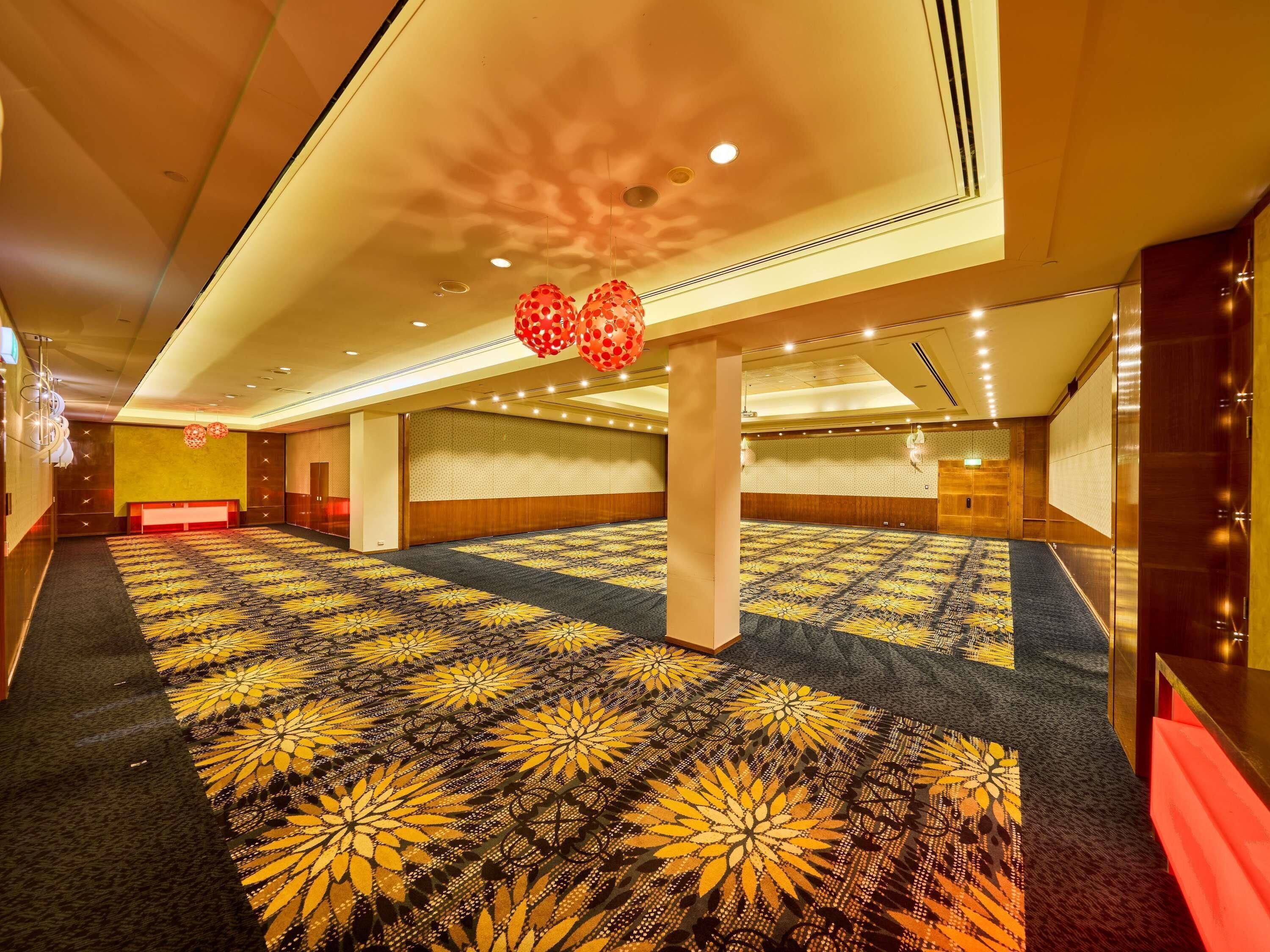A spacious hotel lobby with a patterned carpet, wooden paneling, and a ceiling with recessed lighting.
