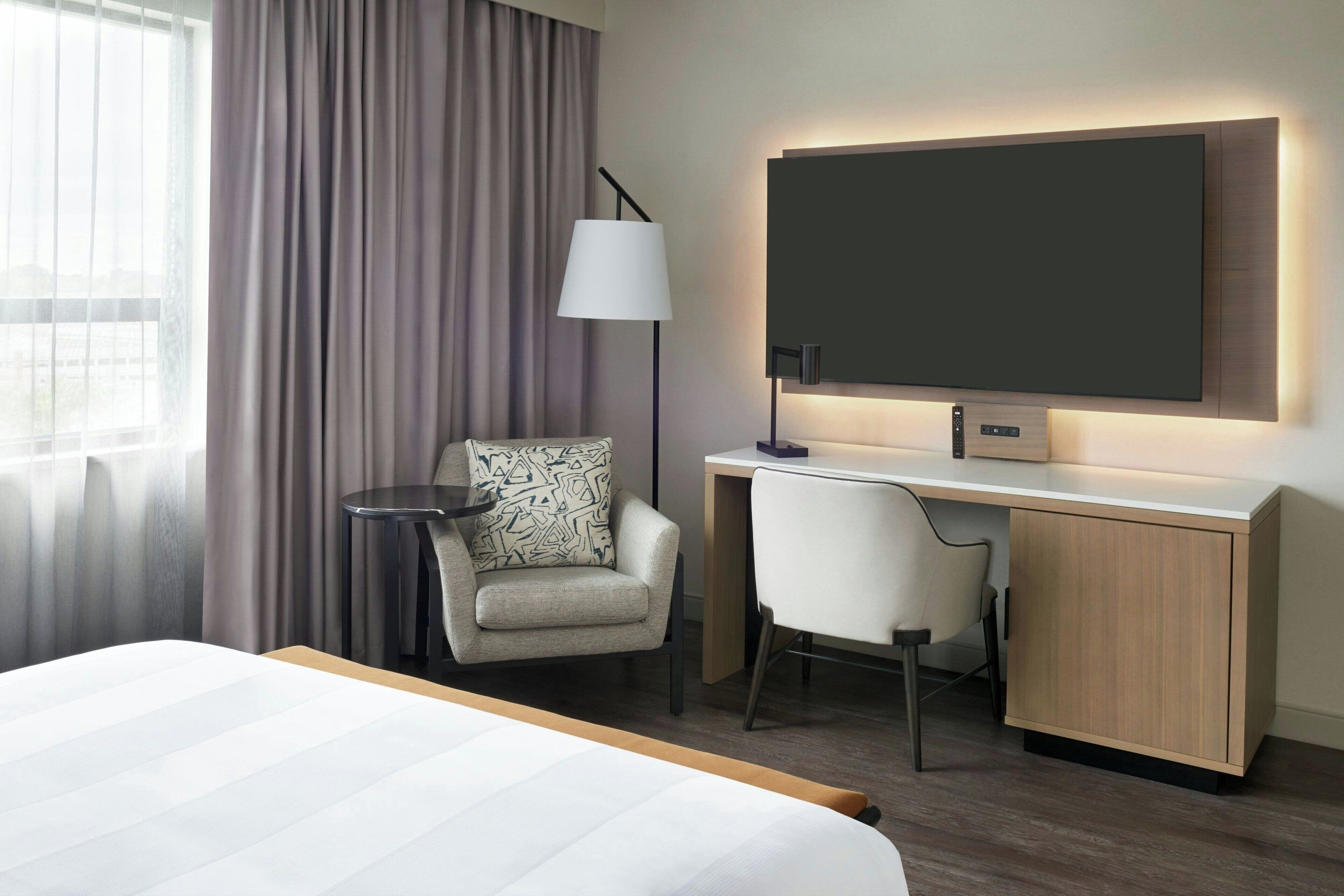 Una habitación de hotel con cama, escritorio, silla, lámpara y televisor.