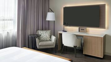 Una habitación de hotel con cama, escritorio, silla, lámpara y televisor.