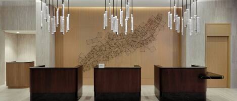 A reception area with three wooden reception desks, a large abstract wall art piece, and hanging light fixtures.