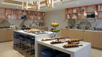 Una cocina moderna con una isla central, taburetes de bar, estantes de cobre y diversos alimentos.