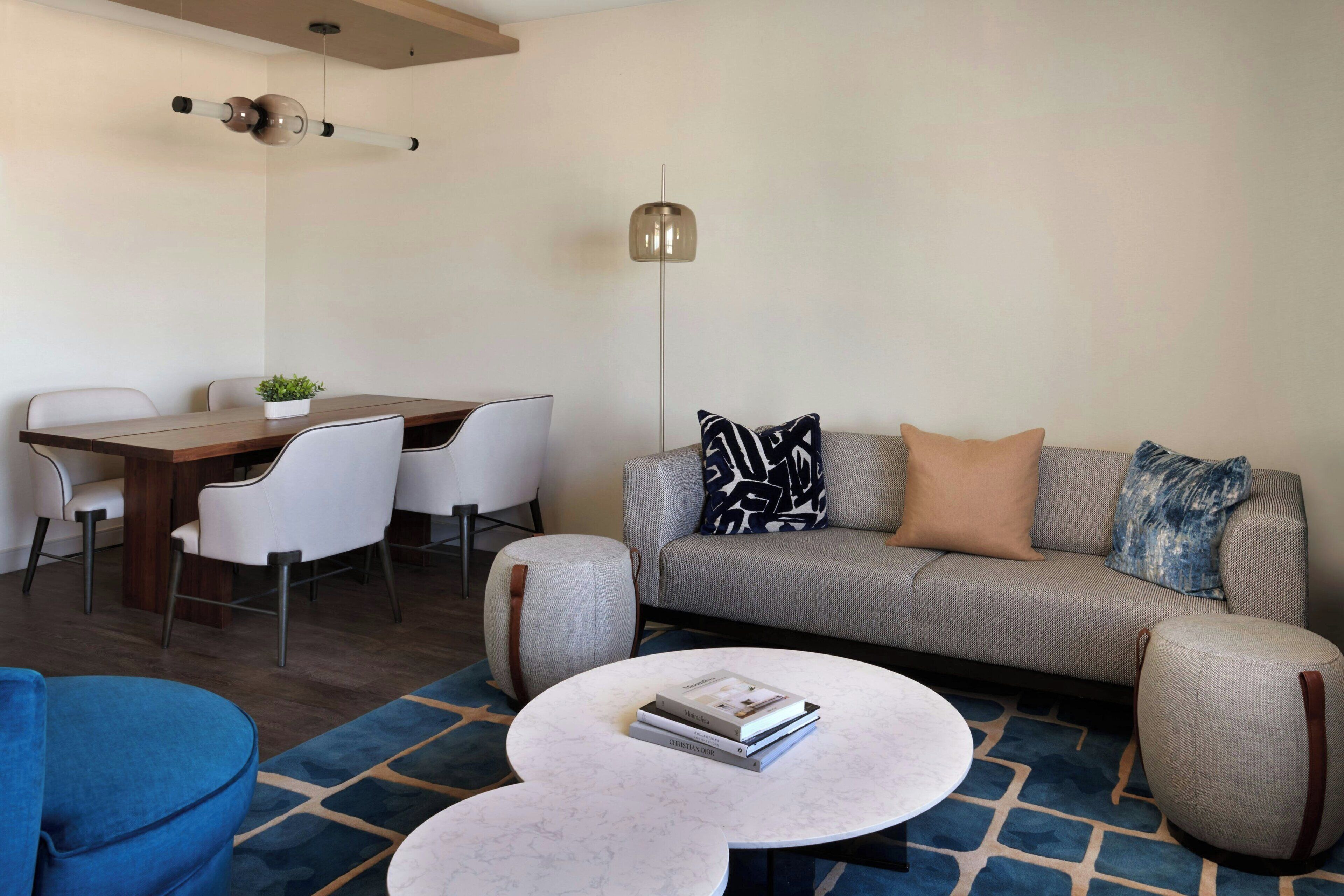 A modern living room with a grey sofa, white chairs, a dining table, and a coffee table with books.