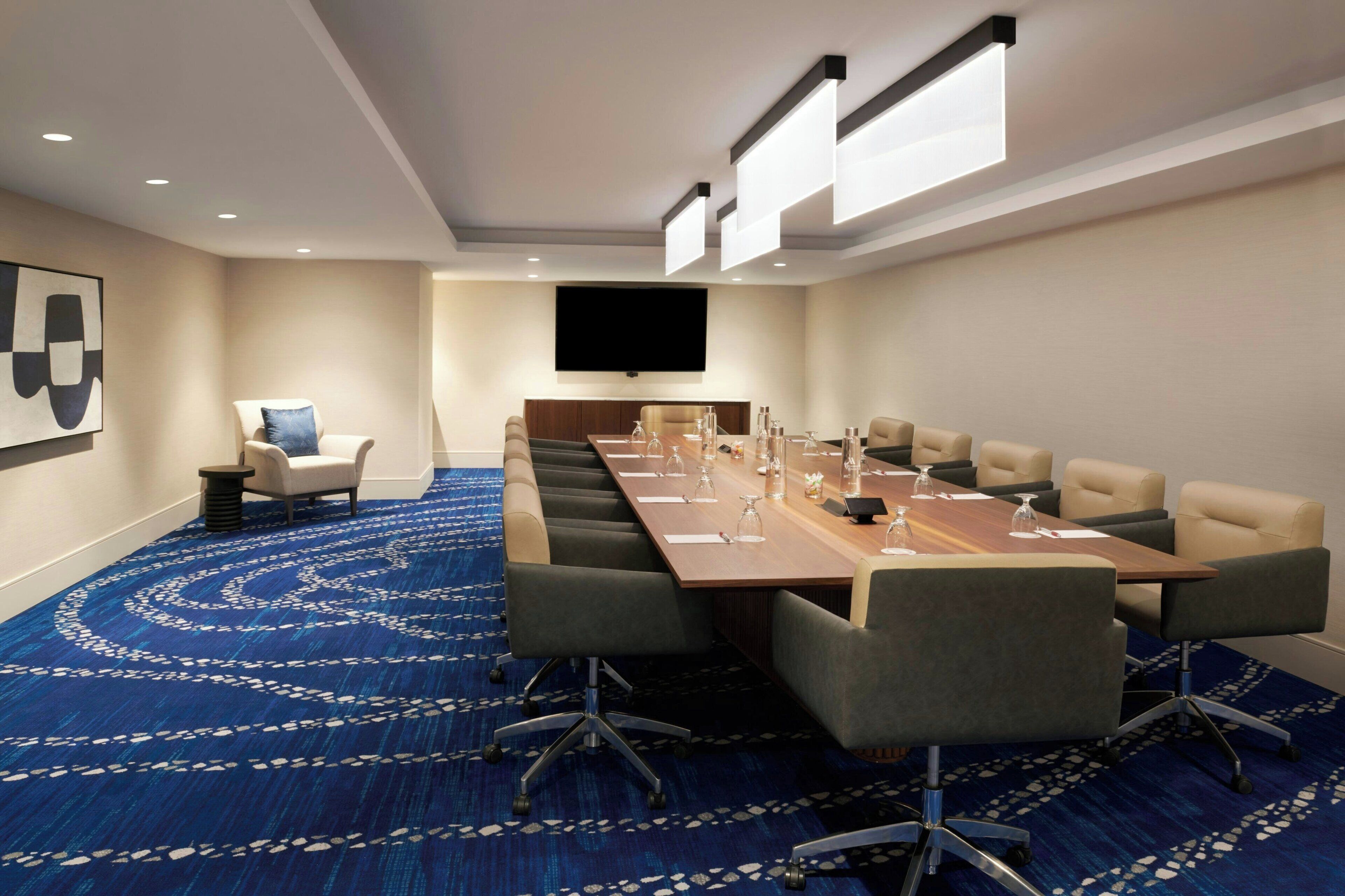 Une salle de conférence avec une longue table, de nombreuses chaises, un téléviseur et une moquette à motifs.