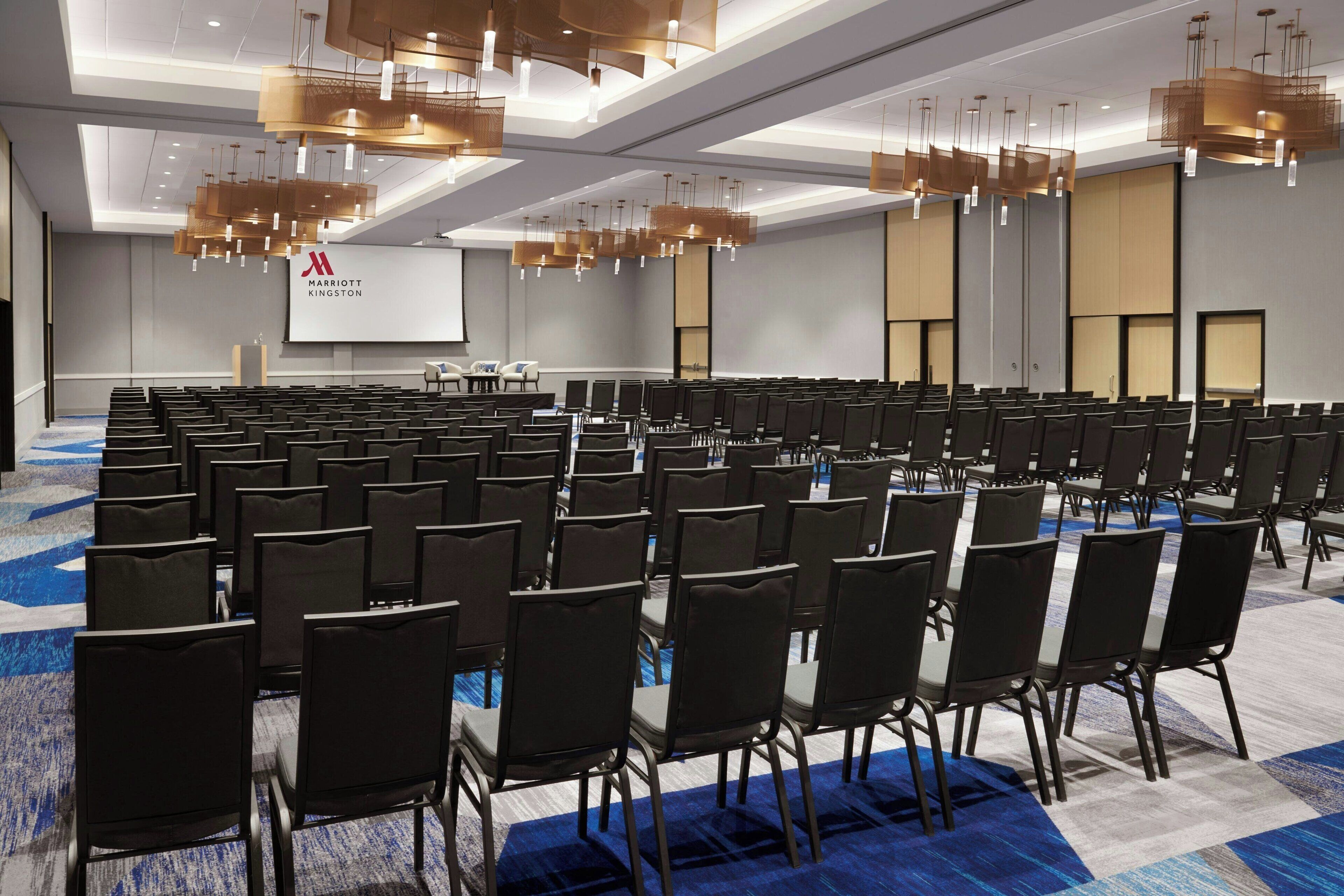 A conference room with rows of chairs, a large screen, and modern lighting fixtures.