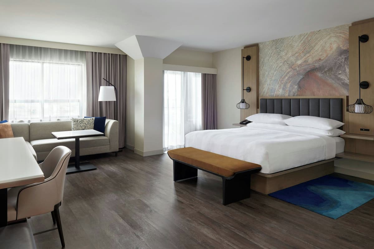 Una habitación de hotel moderna con una cama grande, un sofá, un escritorio y un banco.