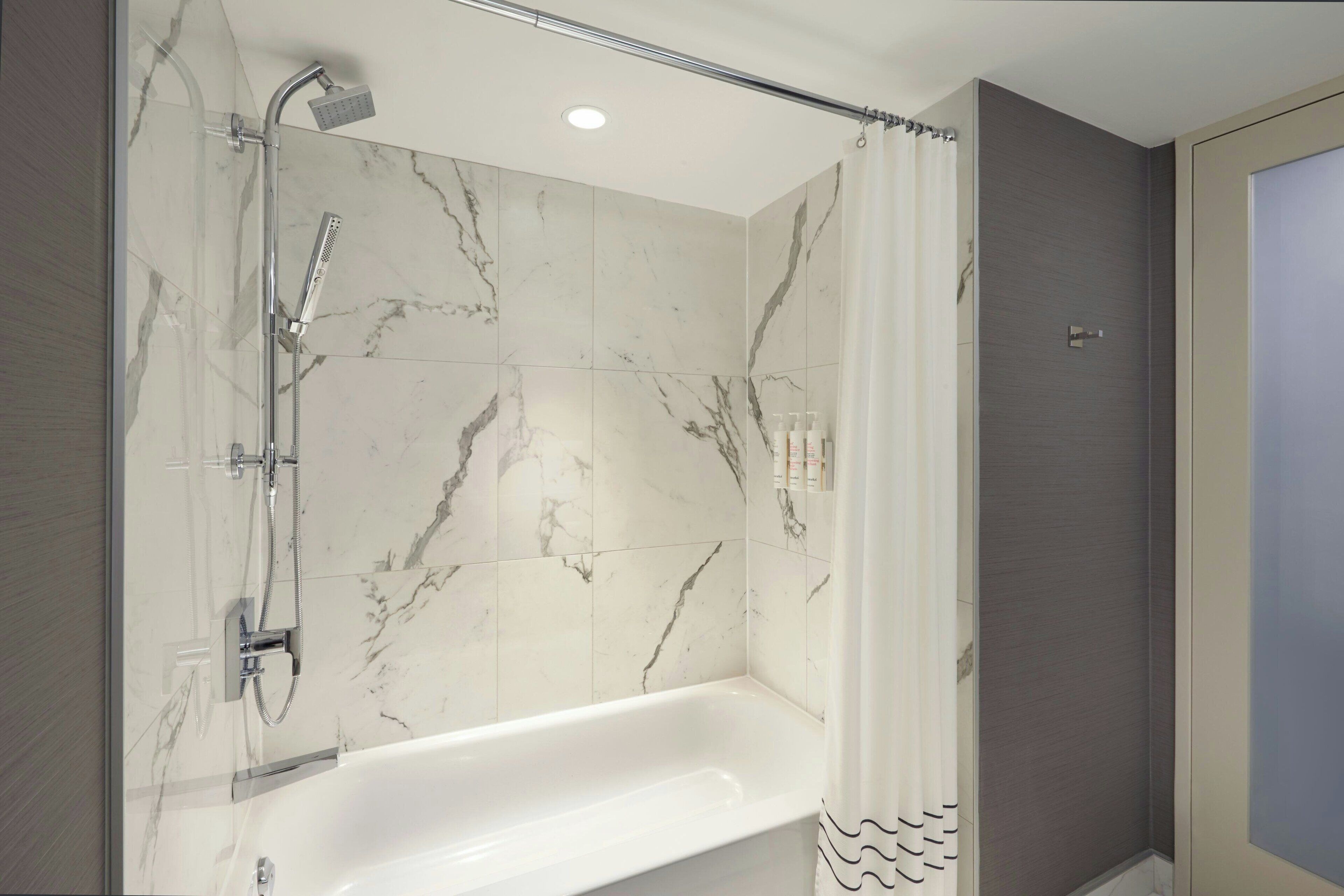 Ein modernes Badezimmer mit einer gläsernen Duschkabine, einer weißen Badewanne und Marmorfliesen.