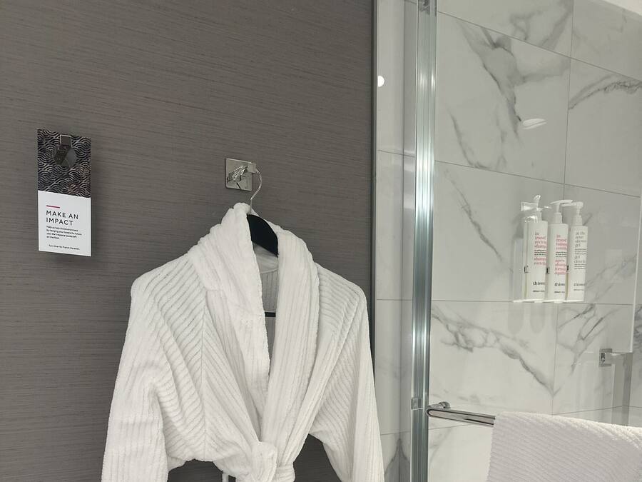A white bathrobe hanging on a hook in a bathroom with a glass shower enclosure and marble tiles.