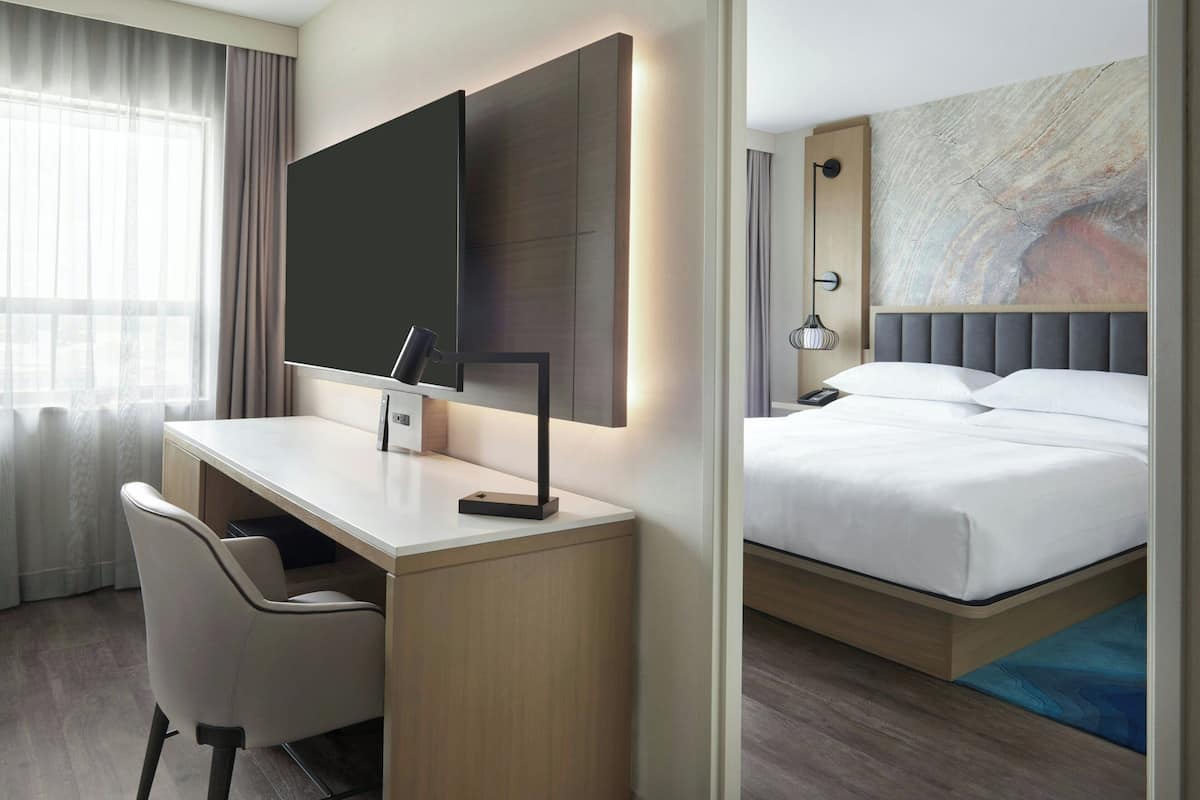 Una habitación de hotel con escritorio, silla, cama y una obra de arte en la pared.