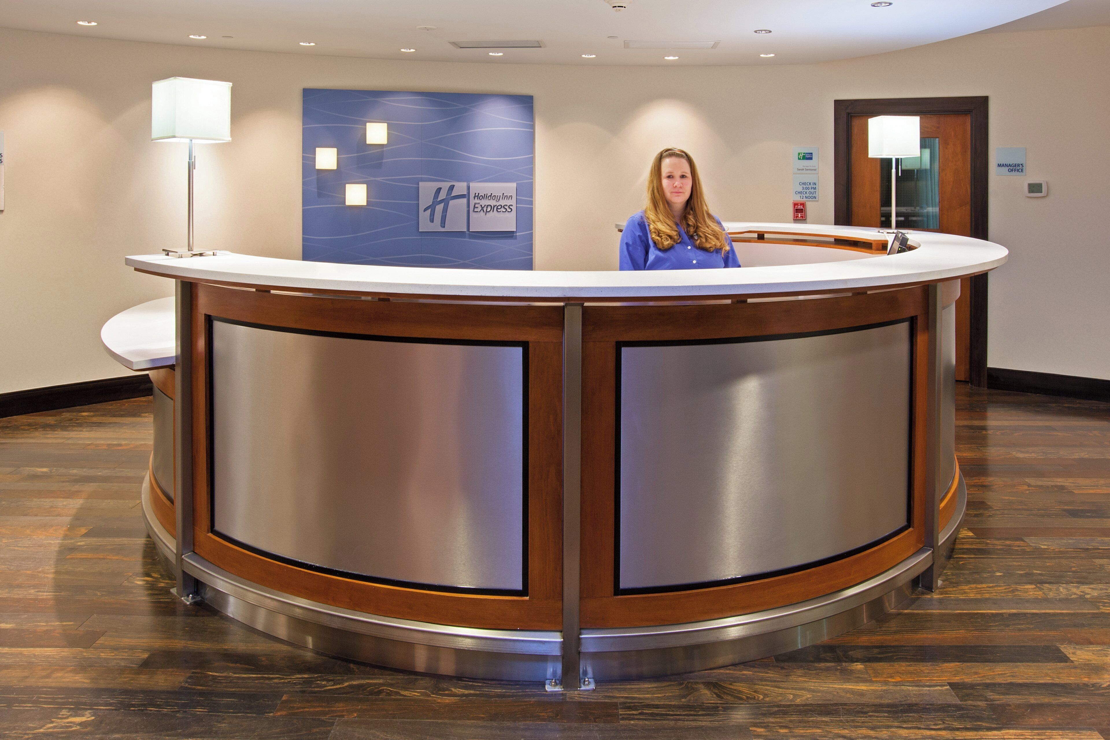 Una reception con un display digitale, una targa con scritto 'Ufficio Direzione' e una segnaletica 'Check-in' che indica gli orari di apertura.