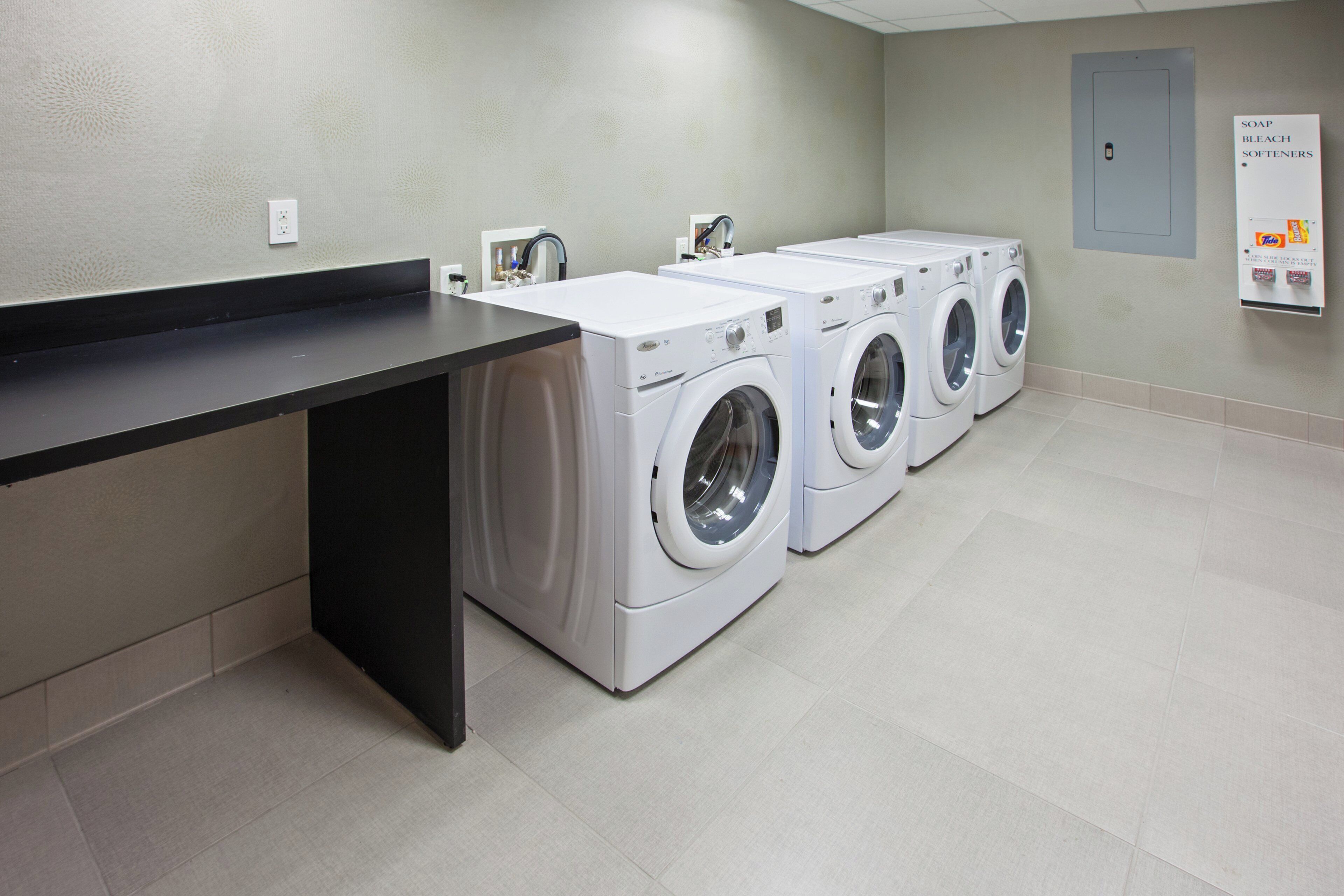 A laundry facility with three front-loading washing machines and a black counter.