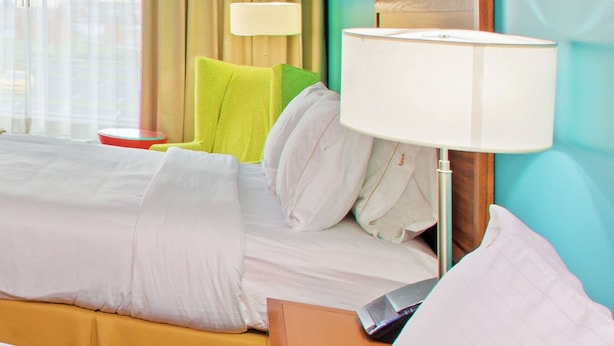 A hotel room with a bed, a nightstand, a lamp, a chair, and a view of the city through the window. - Holiday Inn Express Indianapolis-Fishers by IHG (Fishers)
