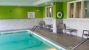 An indoor swimming pool with a lifeguard sign, chairs, and tables around the pool area. - Holiday Inn Express Indianapolis-Fishers by IHG (Fishers)