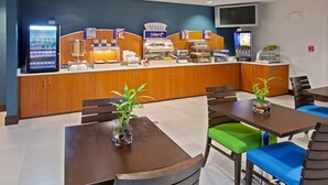 A hotel breakfast area with a self-service counter, a refrigerator, and seating with green and blue chairs. - Holiday Inn Express Indianapolis-Fishers by IHG (Fishers)