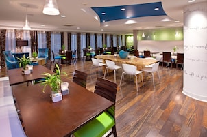 A modern dining area with multiple tables and chairs, a large wooden table in the center, and decorative plants.