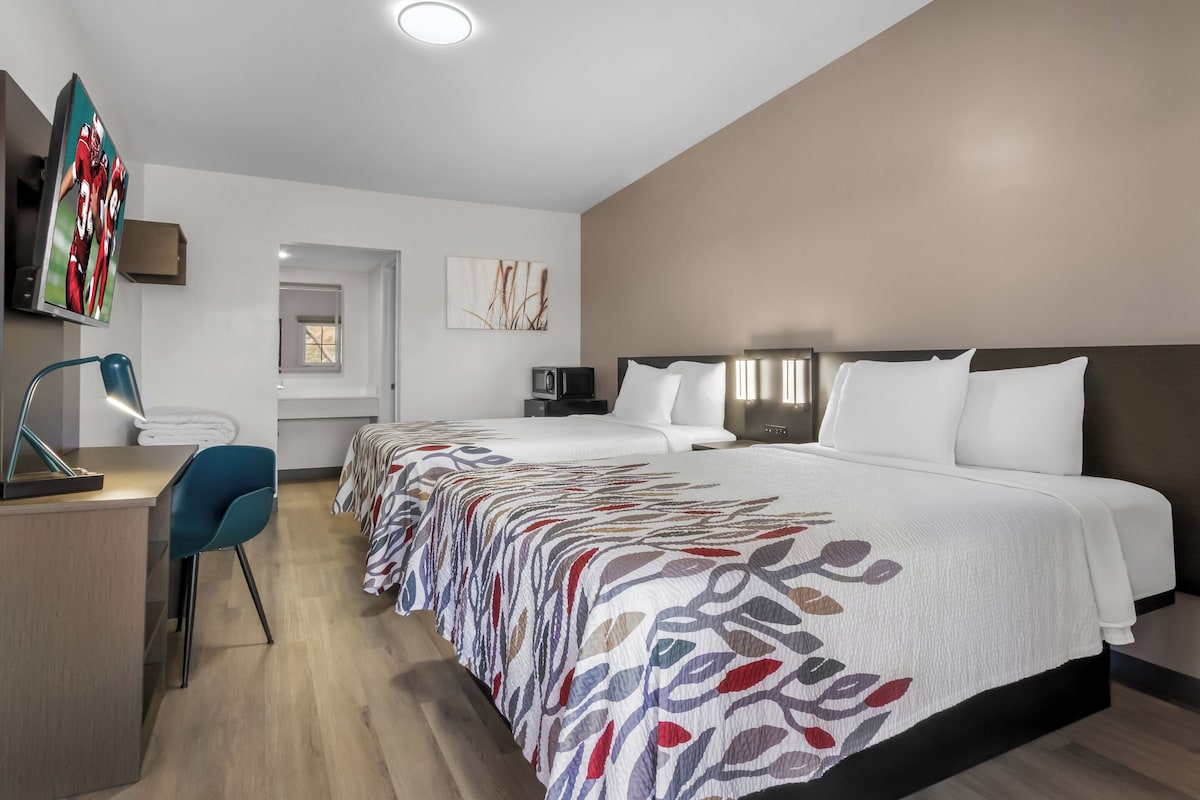 A hotel room with a large bed, a desk with a chair, a television, and a microwave.