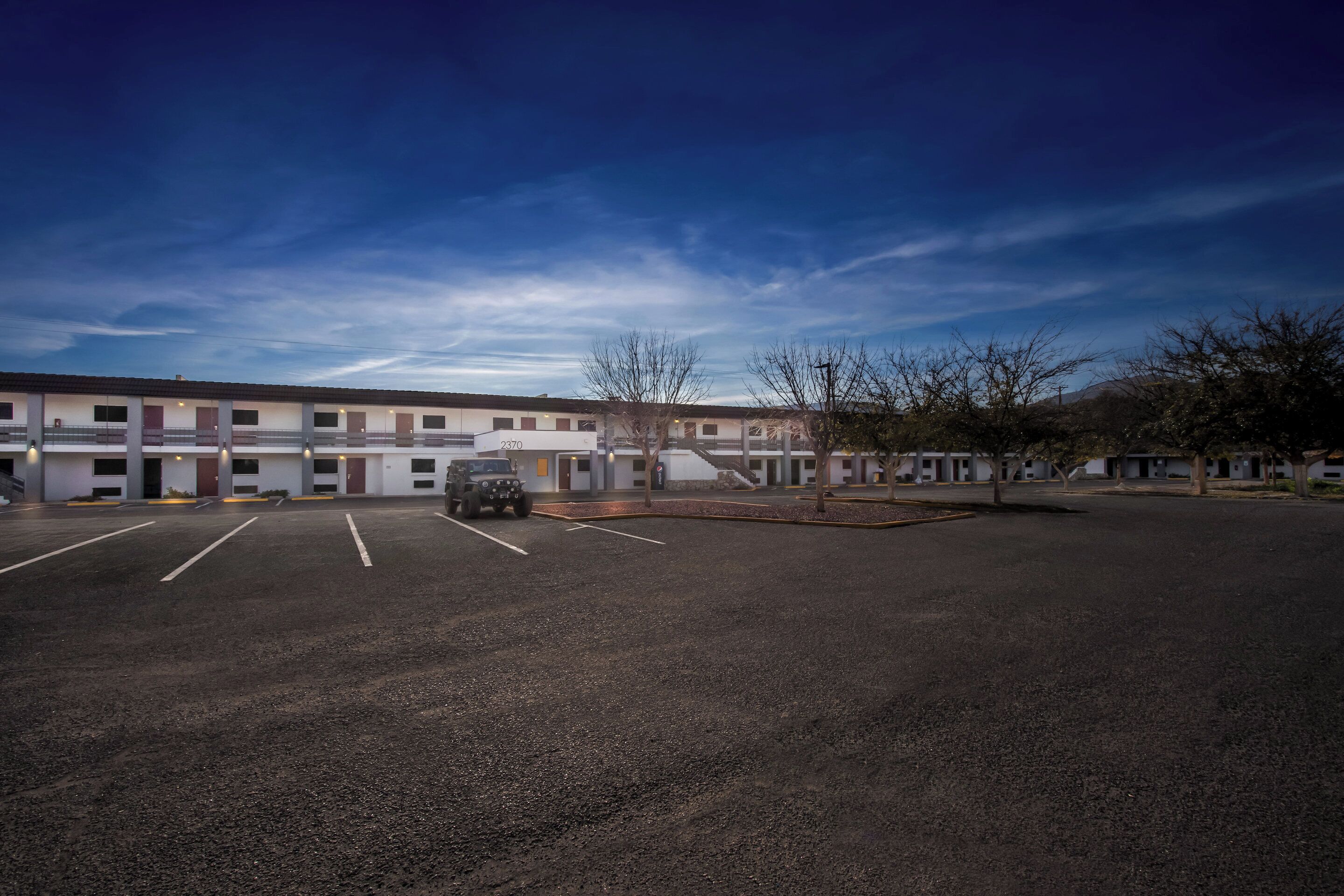 A motel with a parking lot, a building with multiple units, and a clear sky.