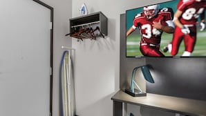 A room with a TV displaying a football game, a coat rack, a desk, and a chair.